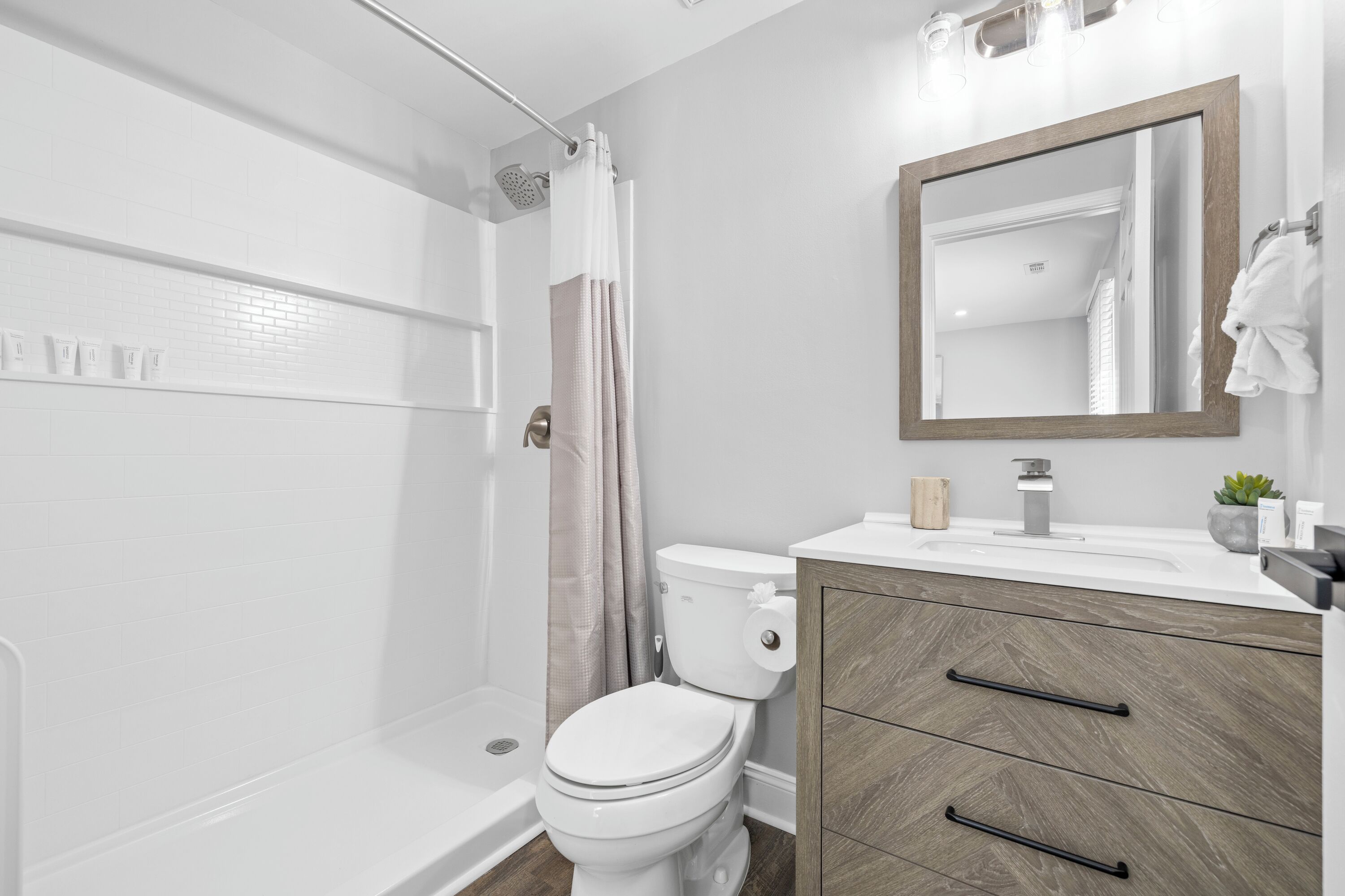 A modern bathroom with a shower, toilet, vanity, and a mirror.