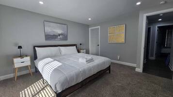 A bedroom with a large bed, a nightstand, a door, and a hallway.