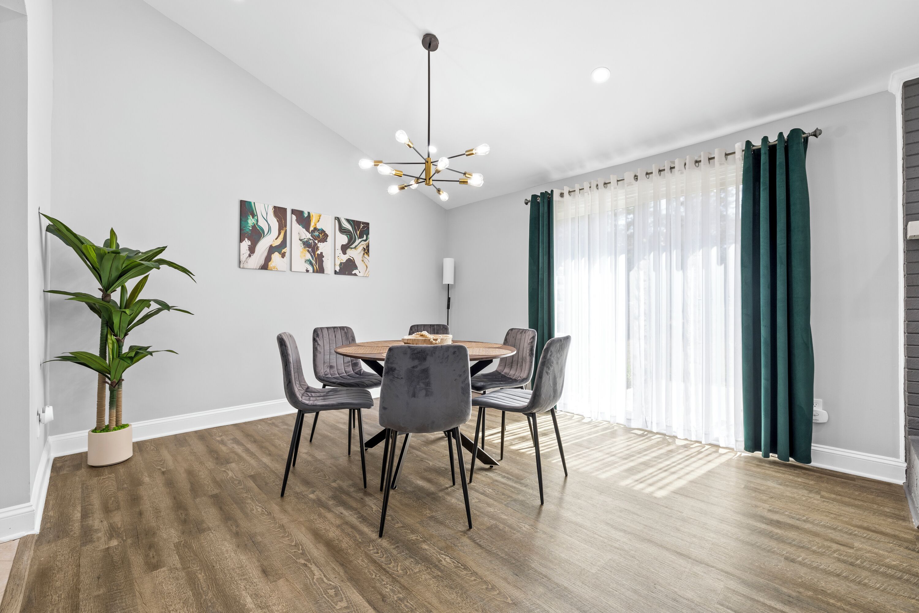 A dining area with a round table, six chairs, a potted plant, and artwork on the wall.