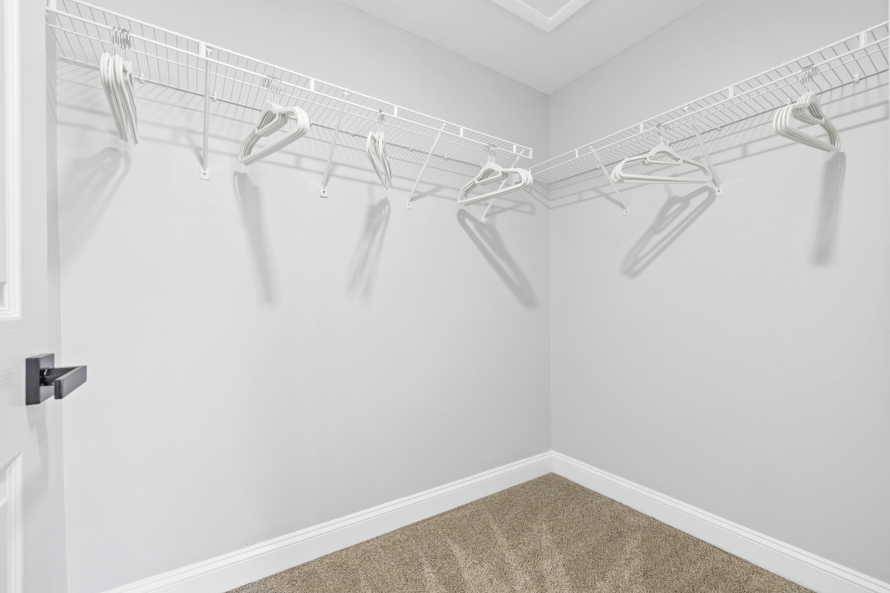Ein Eckzimmer mit weißer Tür, beigeem Teppich und einem Wäscheständer mit mehreren Kleiderbügeln.