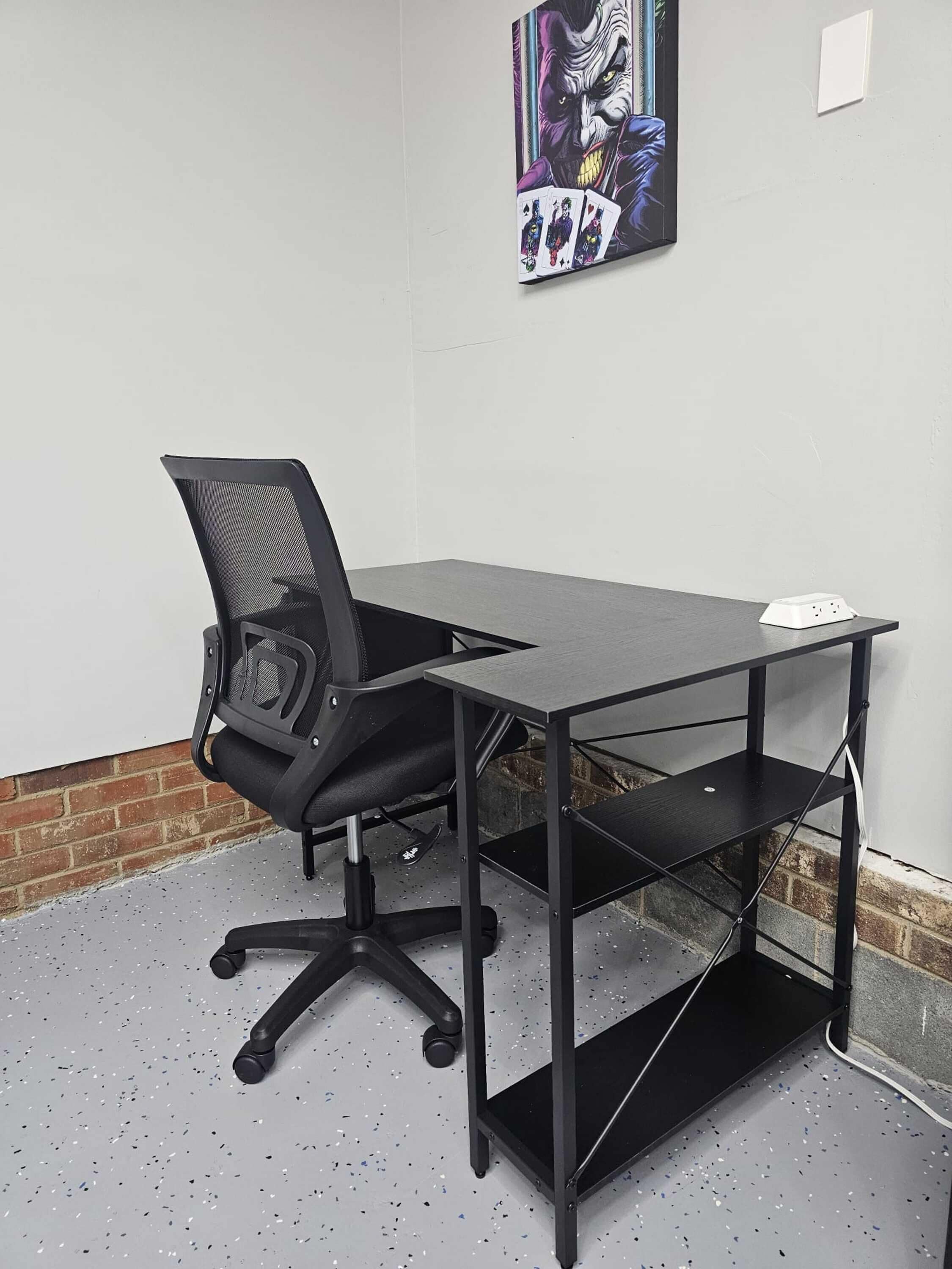 Un espace de travail comprenant une chaise de bureau noire, un bureau noir et un multiprise blanc posé sur le bureau.