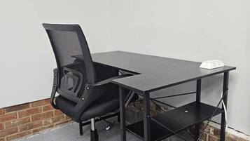 Un espace de travail comprenant une chaise de bureau noire, un bureau noir et un multiprise blanc posé sur le bureau.
