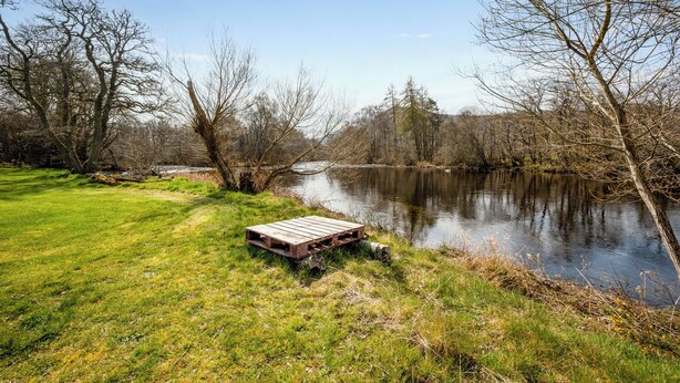 Un entorno junto al río con un muelle de madera y orillas cubiertas de césped.