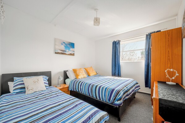 A room with two beds, a desk, a window with curtains, a painting on the wall, and a ceiling light fixture. - 2 Bed Chalet - Sleeps 3 - River and Mountain Views (Strathpeffer)