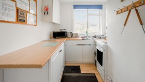 Una cocina compacta con armarios blancos, encimera de madera, microondas, hervidor y ventana con vistas.