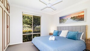 A bedroom with a large bed, a ceiling fan, a painting, and a view through a sliding door.