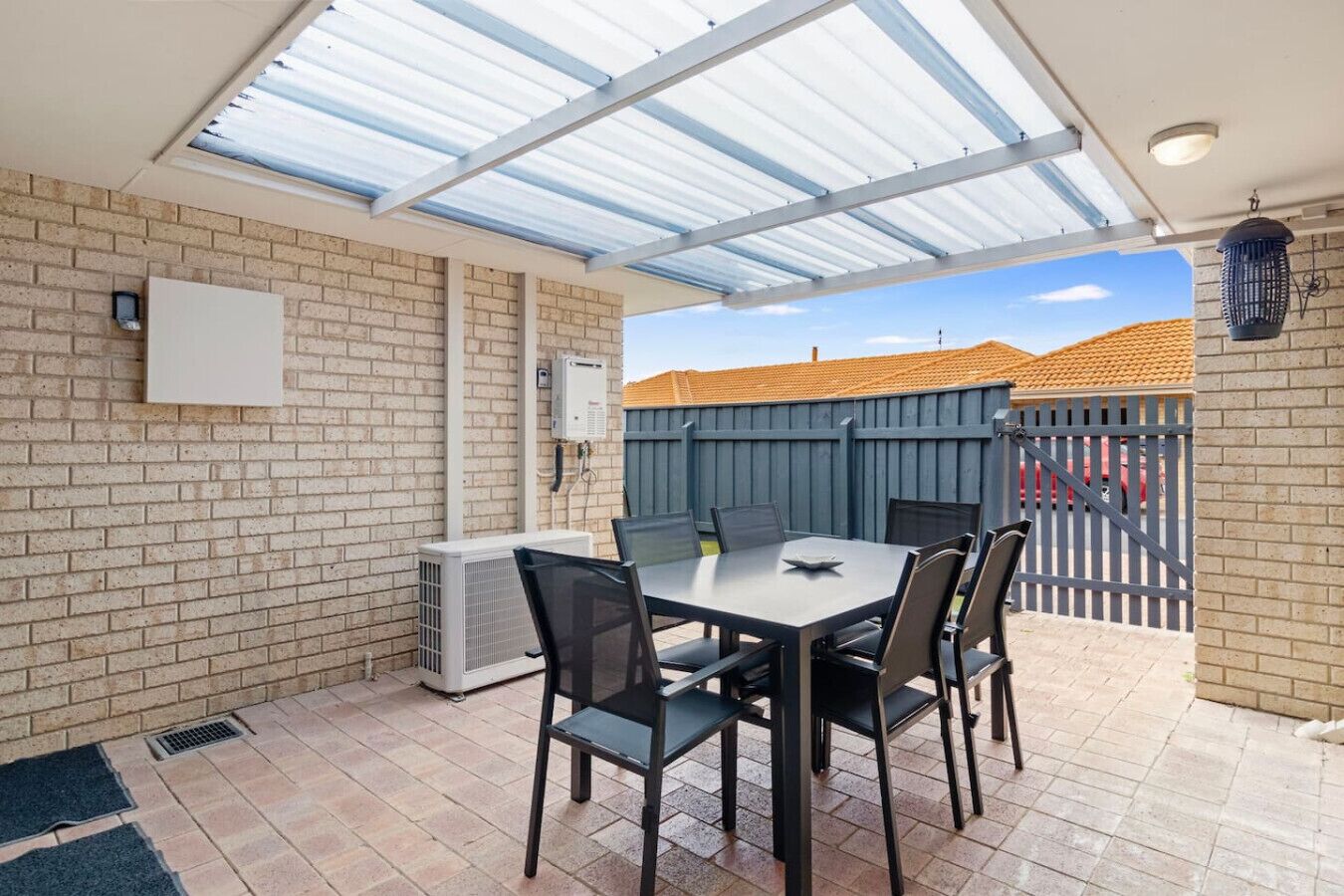 A covered patio with a brick wall, a table with chairs, and a view of a fenced backyard.