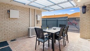 A covered patio with a brick wall, a table with chairs, and a view of a fenced backyard.