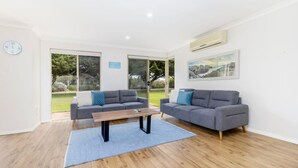 A modern living room with two grey sofas, a wooden coffee table, and a large window with a view of a green landscape.