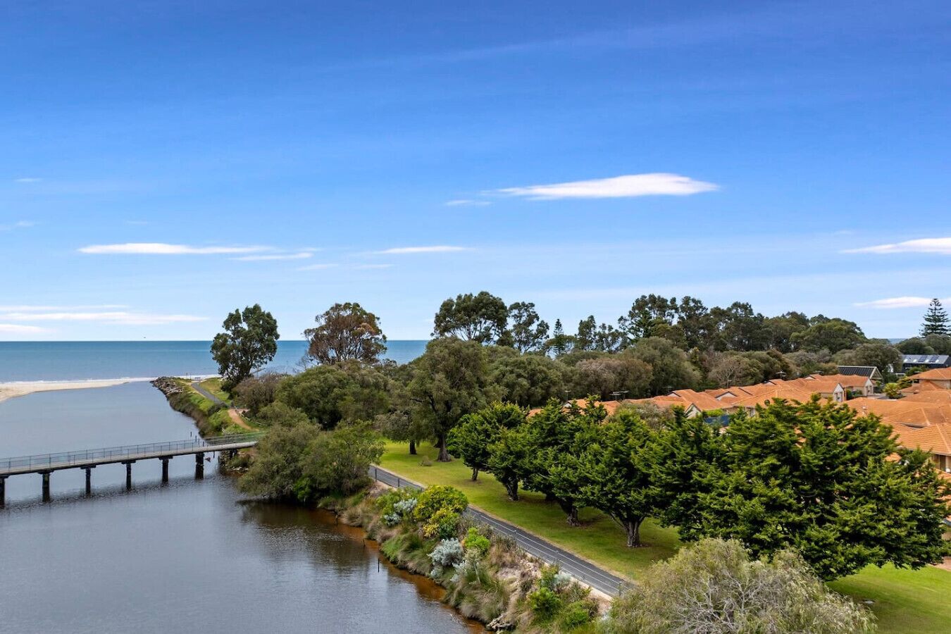 A coastal landscape with a bridge, trees, and buildings with red roofs.