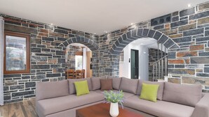 A modern living room with a stone wall, a beige sofa, and a wooden coffee table. - Turtulli Castle Stone Villa 1 - Private Pool Oasis (Hersonissos)