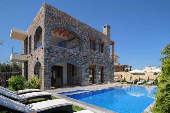 A stone villa with a swimming pool, lounge chairs, and a covered patio area.