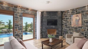 A modern living room with a stone wall, a flat-screen TV, a fireplace, and a view of a swimming pool. - Turtulli Castle Stone Villa 2 - Private Pool Oasis (Hersonissos)