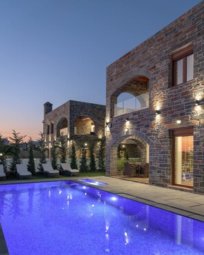 A modern house with a swimming pool, stone walls, and outdoor seating.