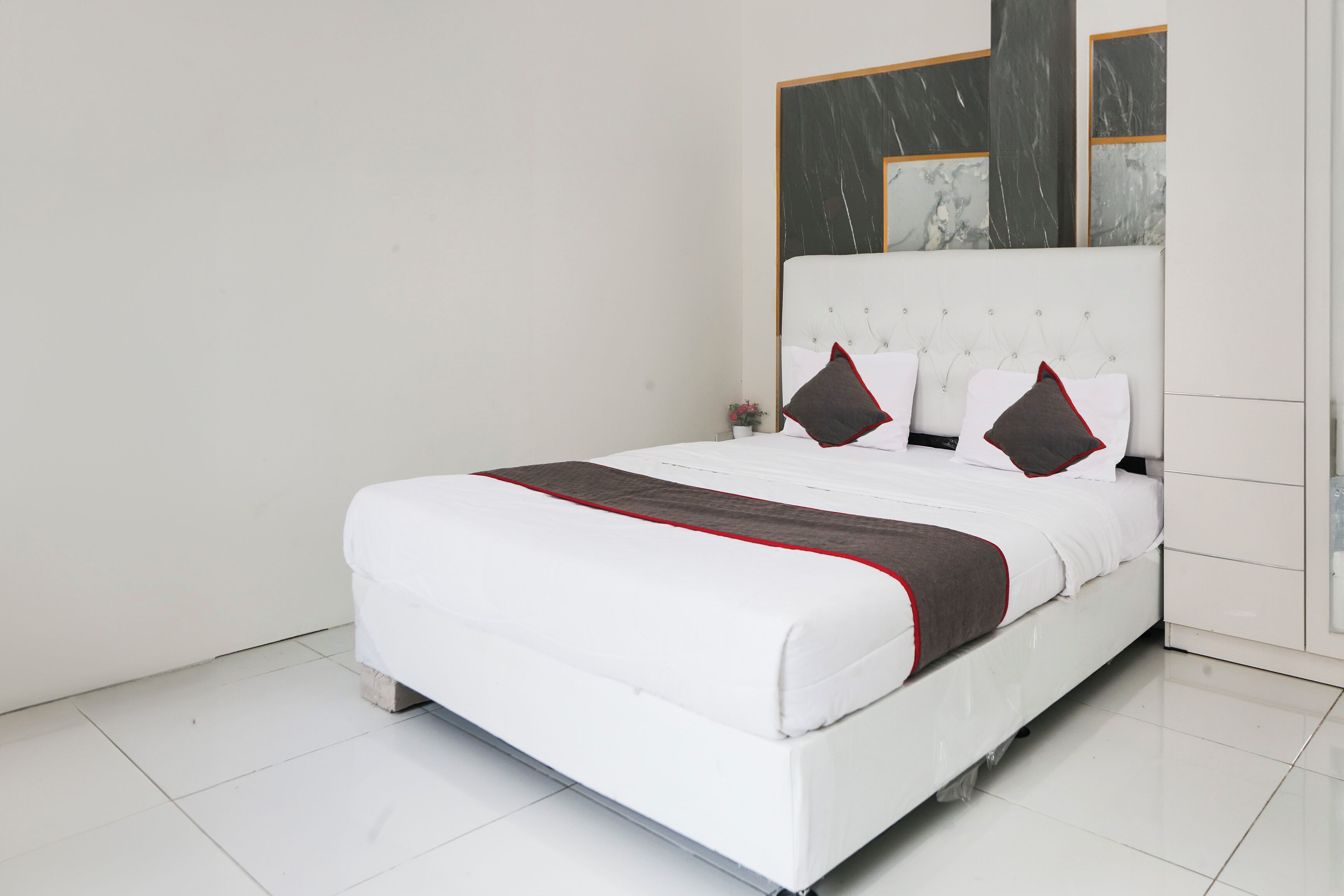 A neatly made bed with white bedding and a brown accent, a small bedside table with a lamp, and a large mirror above the bed.