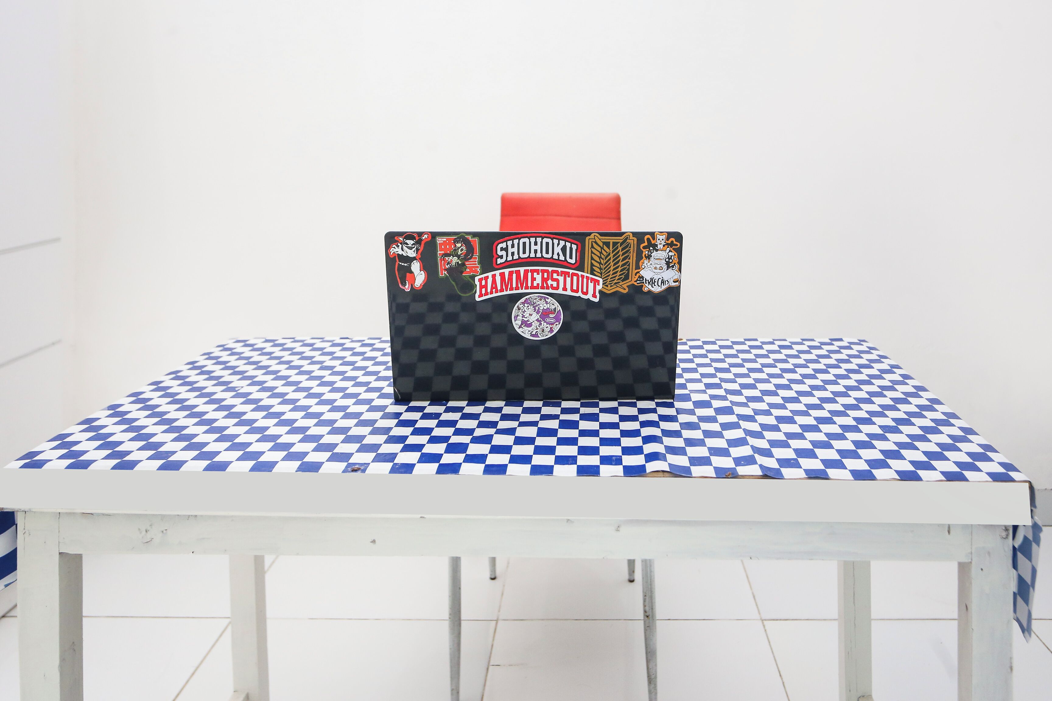 A table with a black and white checkered tablecloth and a black briefcase with red handles and stickers.