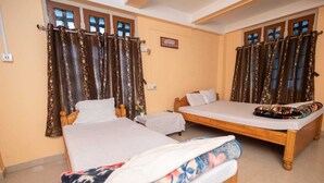 A room with two beds, each with a wooden frame and white bedding. There are curtains on the windows, and a small table with a lamp. - Rhino Cottage Manas By GRB (Barnagar)