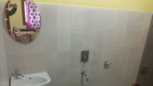 A bathroom with a sink, a mirror, a toilet, and a blue bucket on the floor. - Rhino Cottage Manas By GRB (Barnagar)
