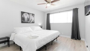 Un dormitorio con cama, ventilador de techo, ventana con cortinas y una obra de arte colgada en la pared.