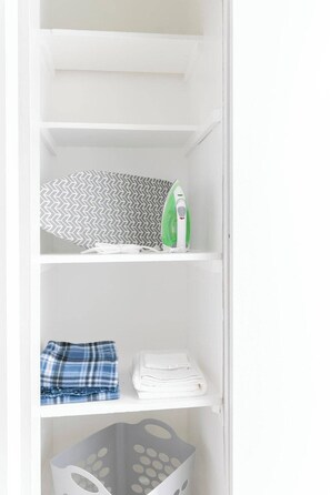 A white shelf with a patterned fabric, a green and white iron, folded towels, and a gray laundry basket. - Chic 2-Bed Oasis, Sleeps 6! Minutes From Strip! (Las Vegas)