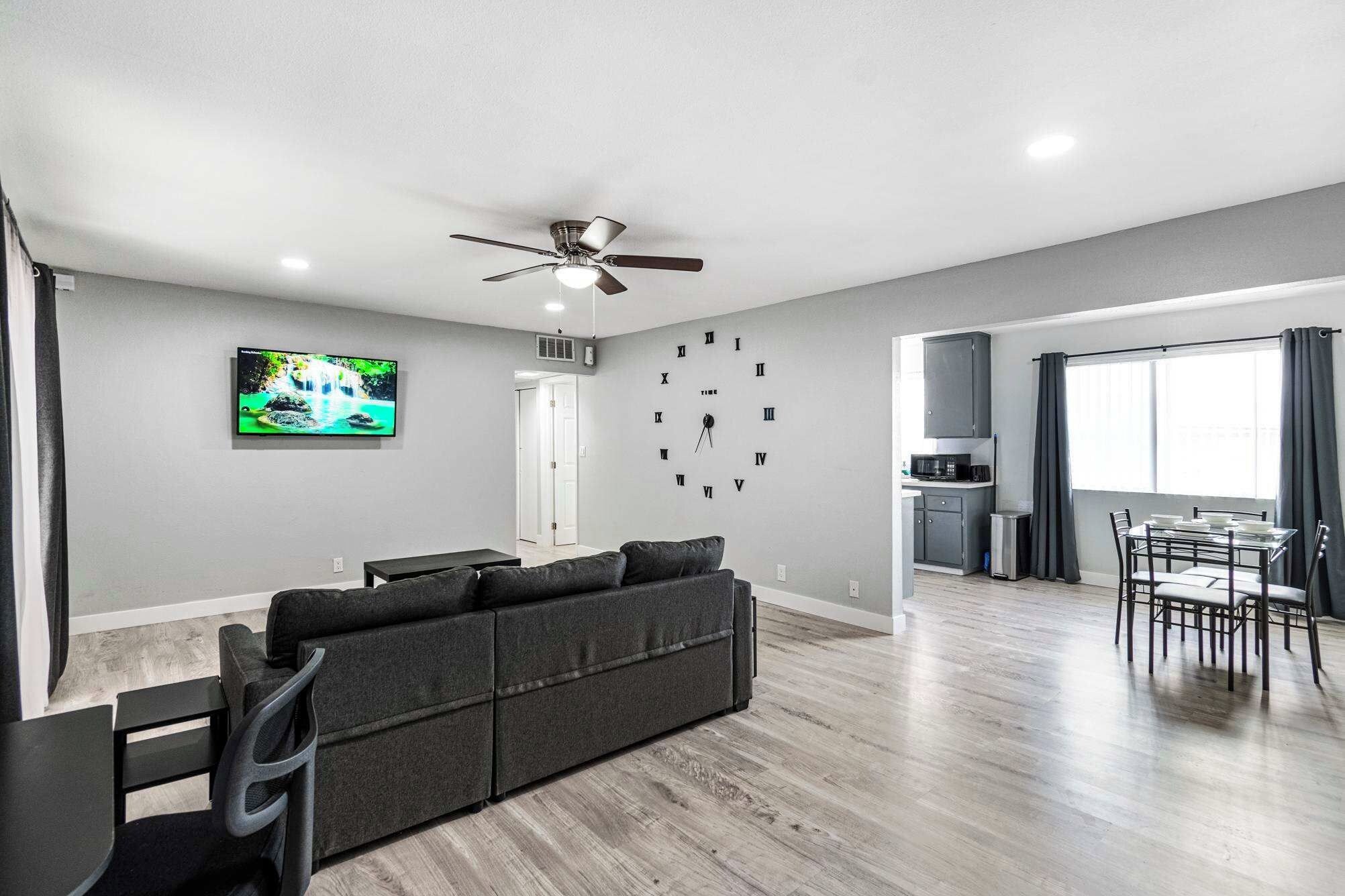 Un salon moderne comprenant un canapé, un téléviseur, un ventilateur de plafond et un coin repas avec des chaises et une table.