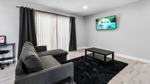 Una sala de estar moderna con un sofá, una mesa de centro, un televisor montado en la pared y un ventilador de techo.