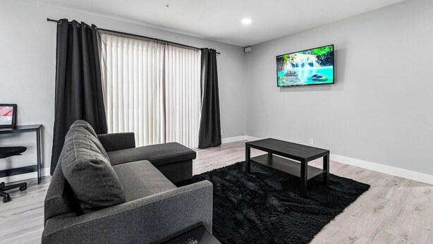 A modern living room with a sofa, a coffee table, a TV mounted on the wall, and a ceiling fan.
