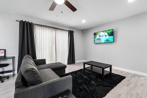 A modern living room with a sofa, a coffee table, a TV mounted on the wall, and a ceiling fan. - Chic 2-Bed Oasis, Sleeps 6! Minutes From Strip! (Las Vegas)