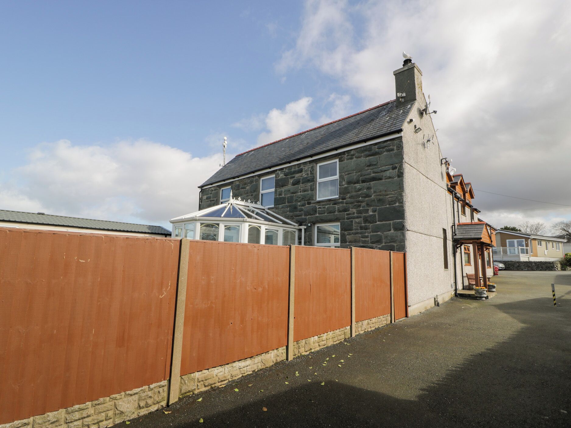 A residential building with a stone facade, a conservatory, and a wooden fence.