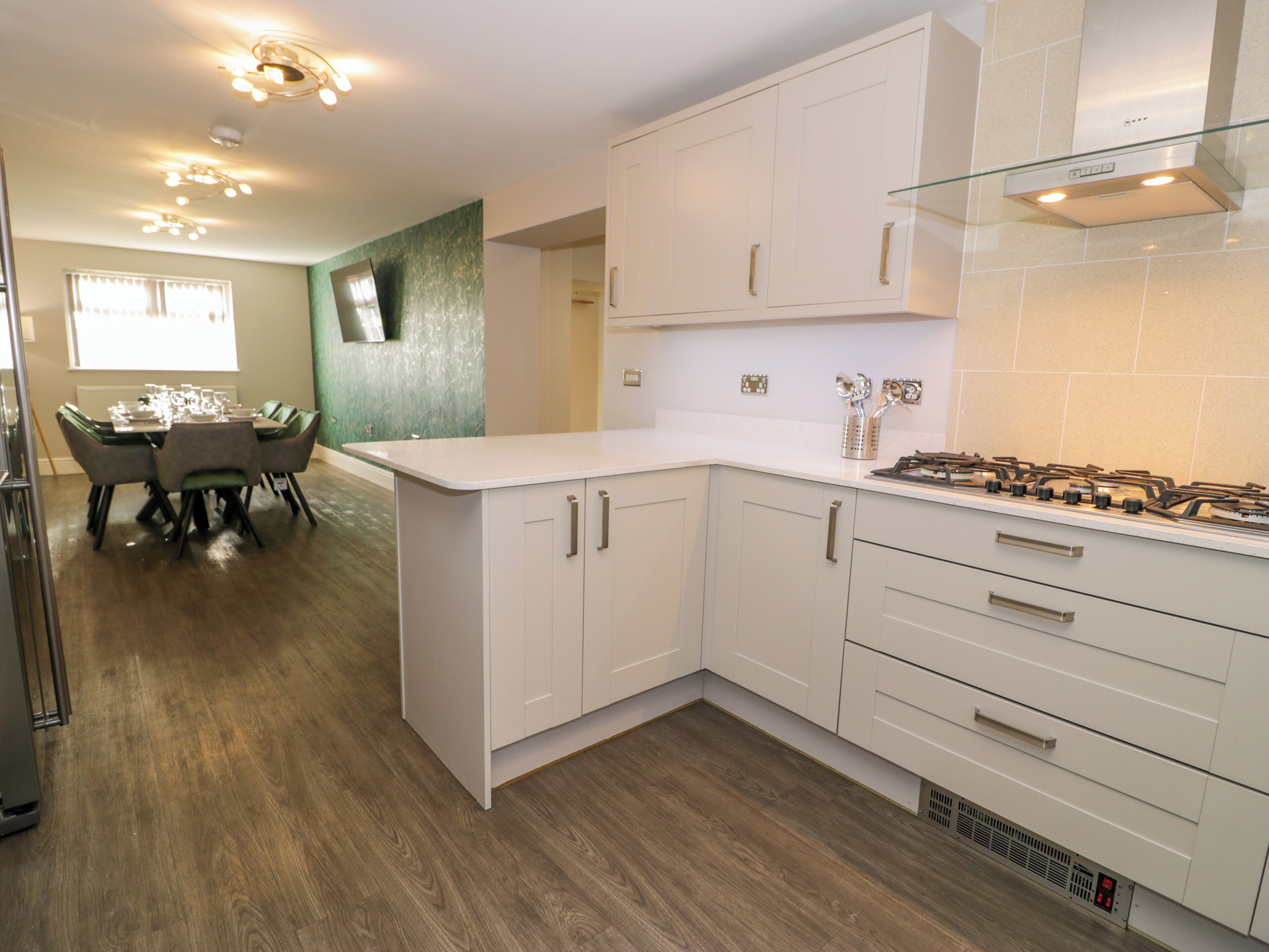 Una cocina moderna con armarios blancos, extractor de acero inoxidable y un comedor con mesa y sillas.