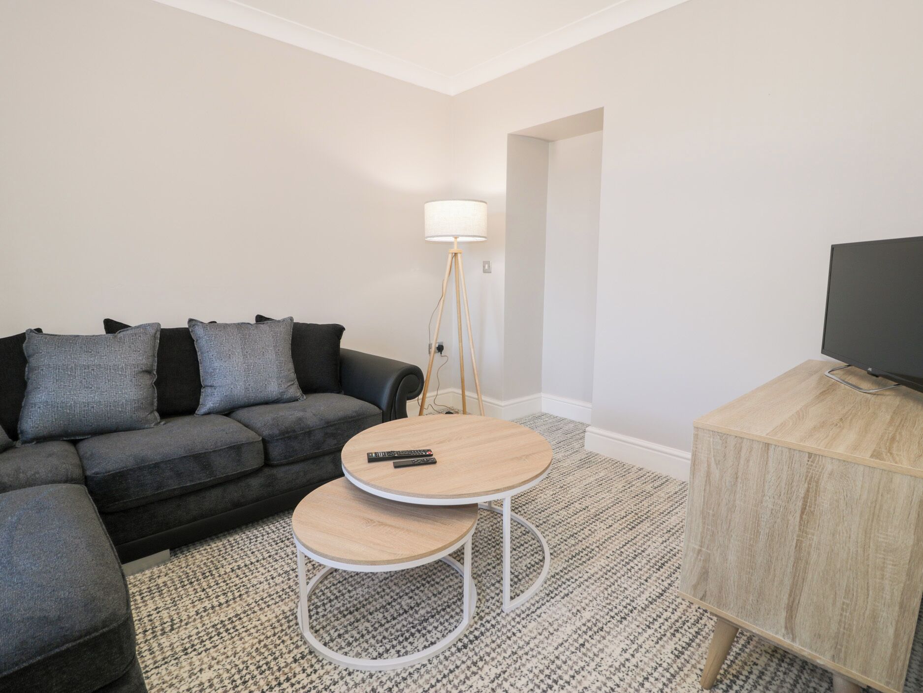 A modern living room with a grey sofa, two round wooden tables, a floor lamp, and a TV stand.