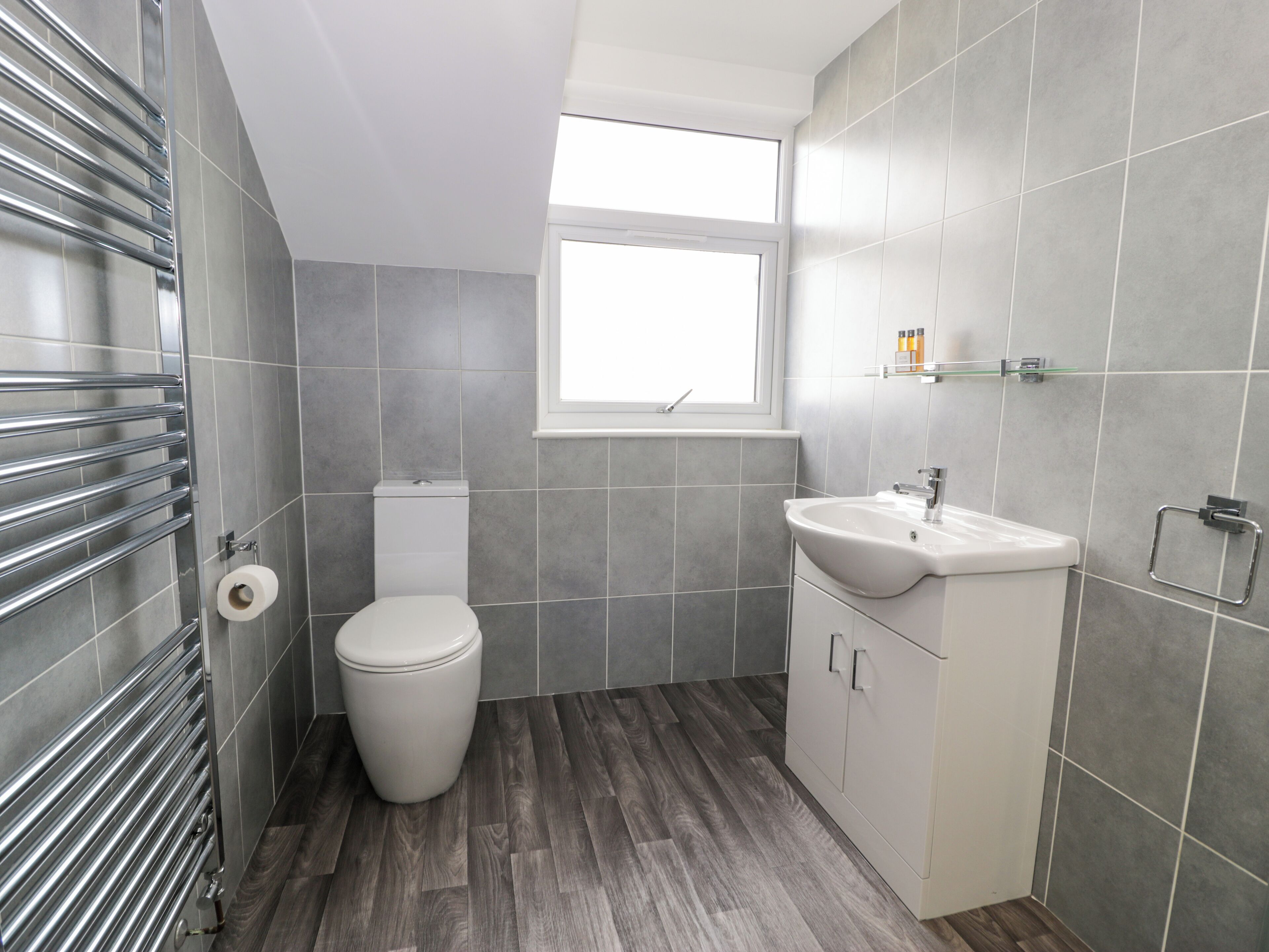 A modern bathroom with grey tiles, a toilet, a sink, and a window.