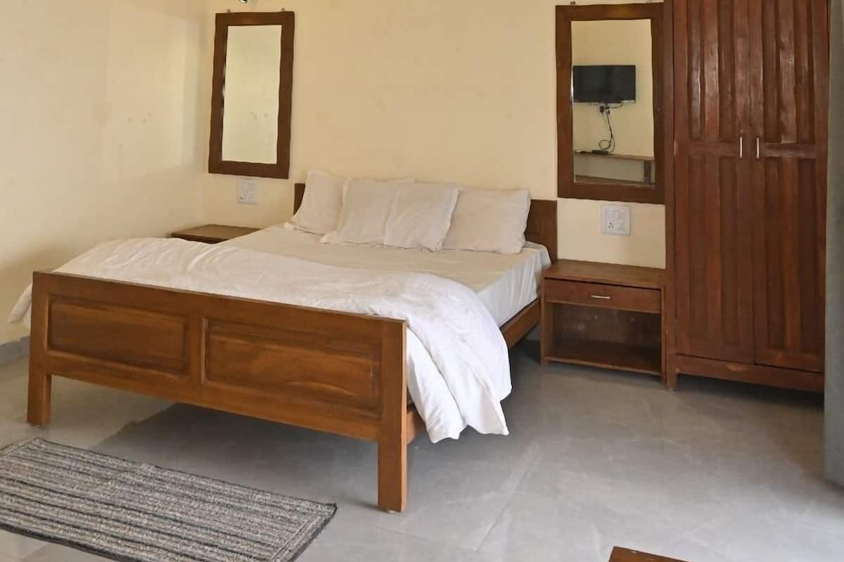Une chambre avec un lit en bois, un ventilateur de plafond, une armoire en bois et une petite table de chevet.