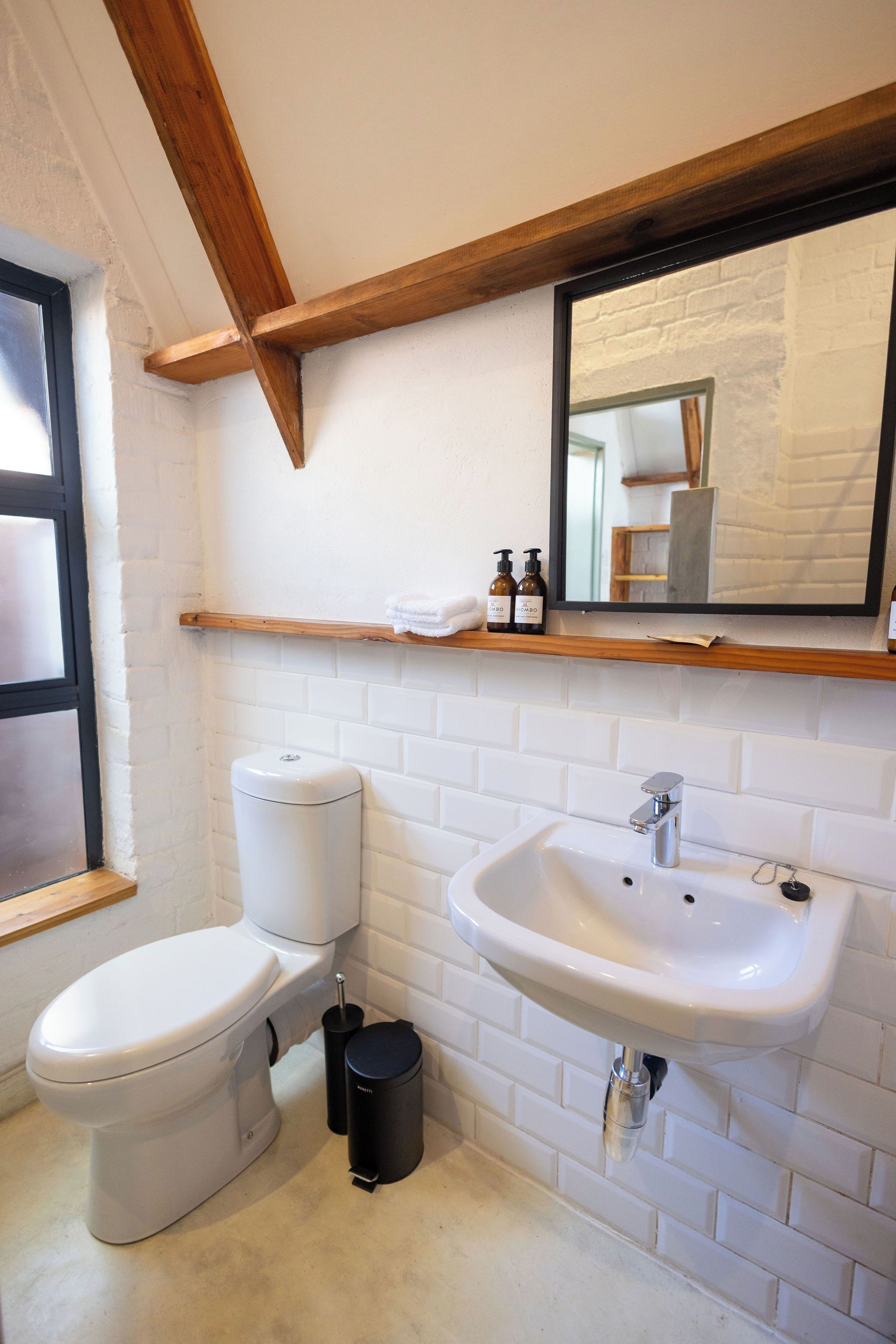 A compact bathroom with a white toilet, a white sink, and a black trash bin.