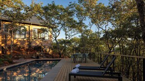 A wooden deck with a pool, lounge chairs, and a table.