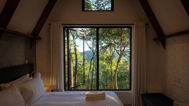 A bedroom with a large window, a bed, a bedside table, and a bench.