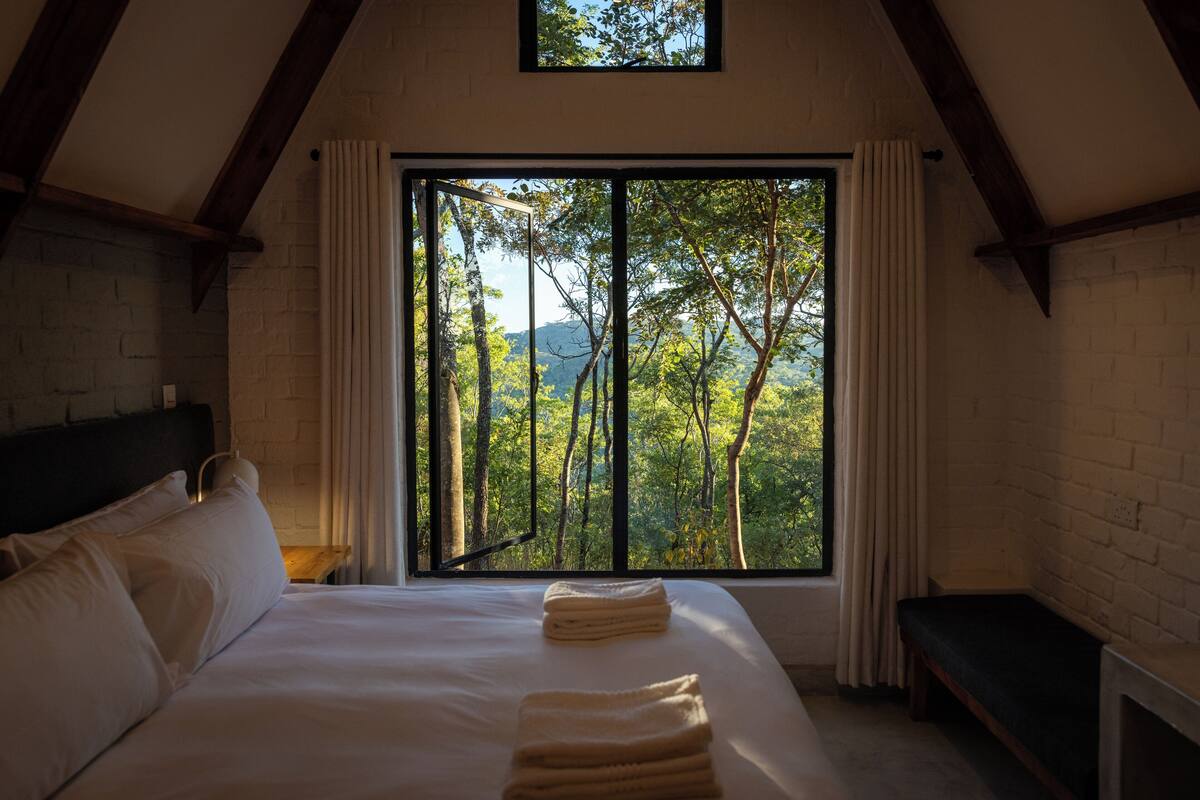 Ein Schlafzimmer mit großem Fenster, einem Bett, einem Nachttisch und einer Bank.