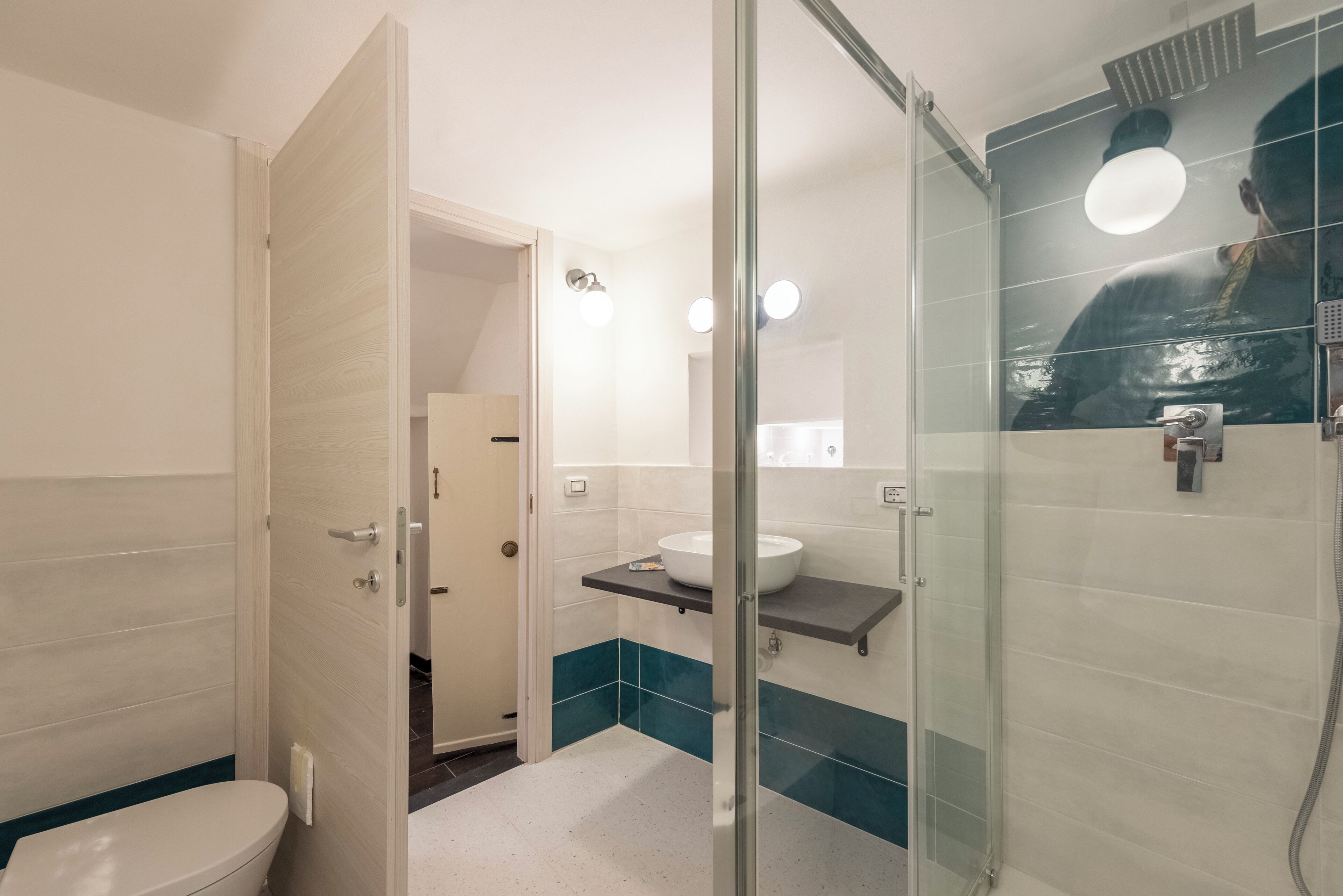 A modern bathroom with a glass shower enclosure, a white sink, and a mirror with a round light.