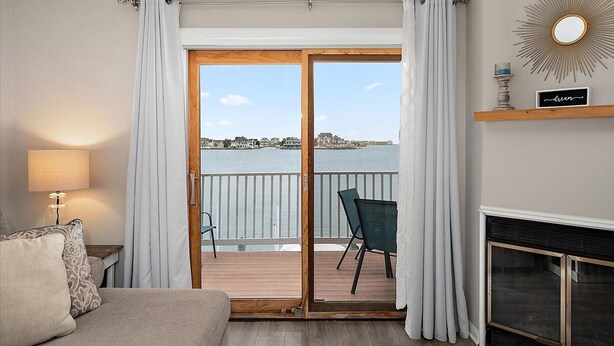 A room with a view of the sea, a sofa, a lamp, a fireplace, and a mirror on the wall.