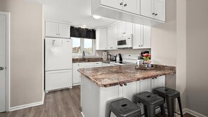 A modern kitchen with white cabinetry, a granite countertop, and a central island with bar stools.