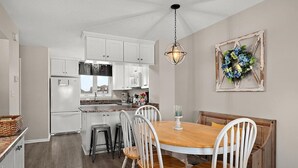 A kitchen with white cabinets, a wooden dining table with four chairs, and a hanging light fixture.