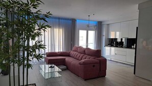 Una sala de estar moderna con un sofá modular, una mesa de centro de vidrio y una planta de bambú grande.