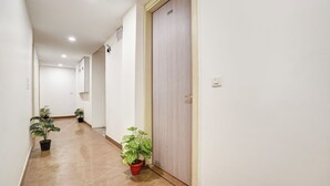 A hallway with a tiled floor, potted plants, and a wooden door. - Breezy Height (New Delhi)