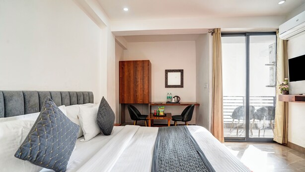 A hotel room with a bed, a desk, a chair, and a sliding glass door to the balcony. - Breezy Height (New Delhi)