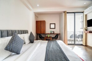 Ein Hotelzimmer mit einem Bett, einem Schreibtisch, einem Stuhl und einer Schiebeglastür zum Balkon.