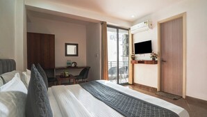 A hotel room with a bed, a desk, a TV, and a balcony with a view. - Breezy Height (New Delhi)