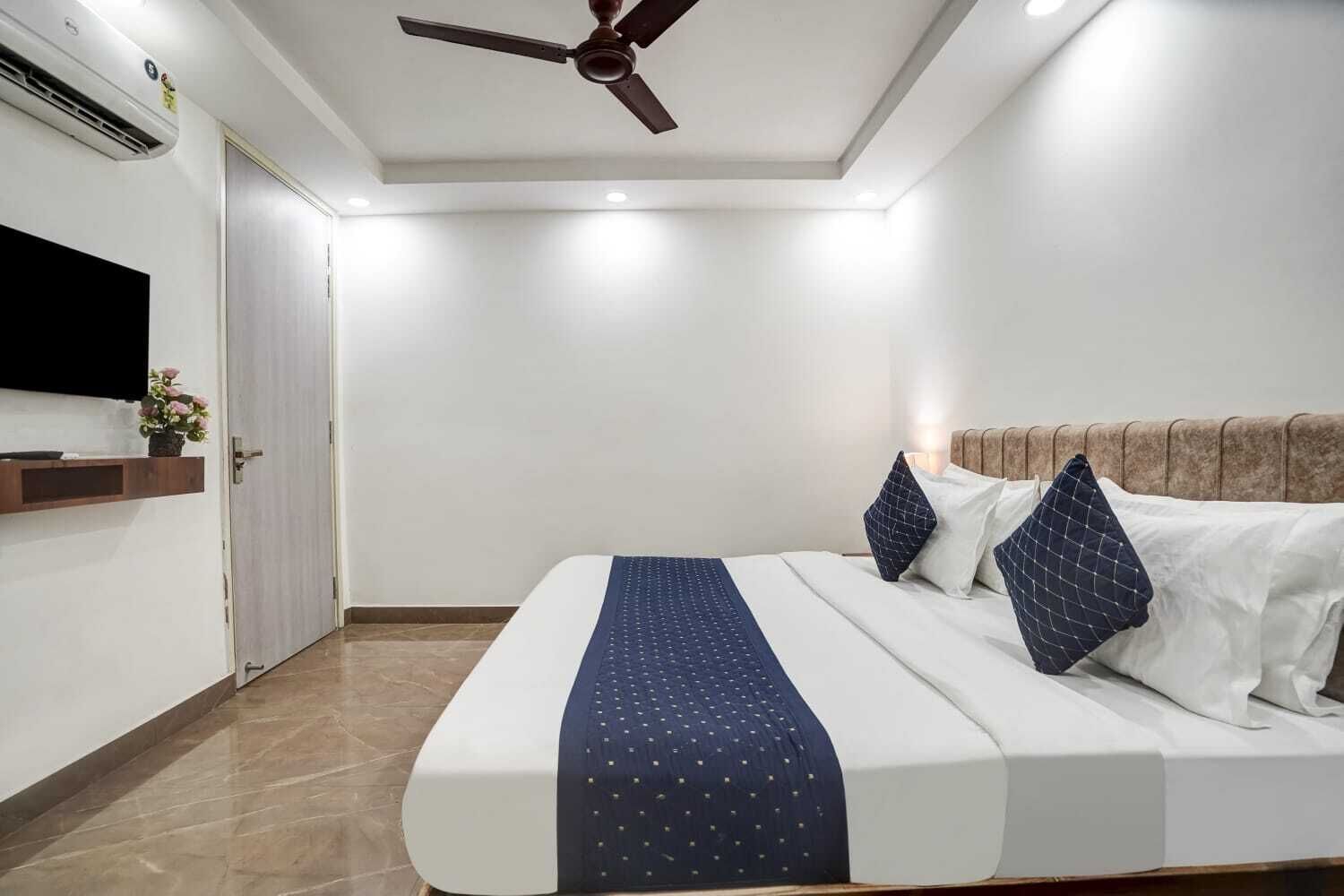 A hotel room with a bed, a ceiling fan, a TV mounted on the wall, and a wooden headboard.