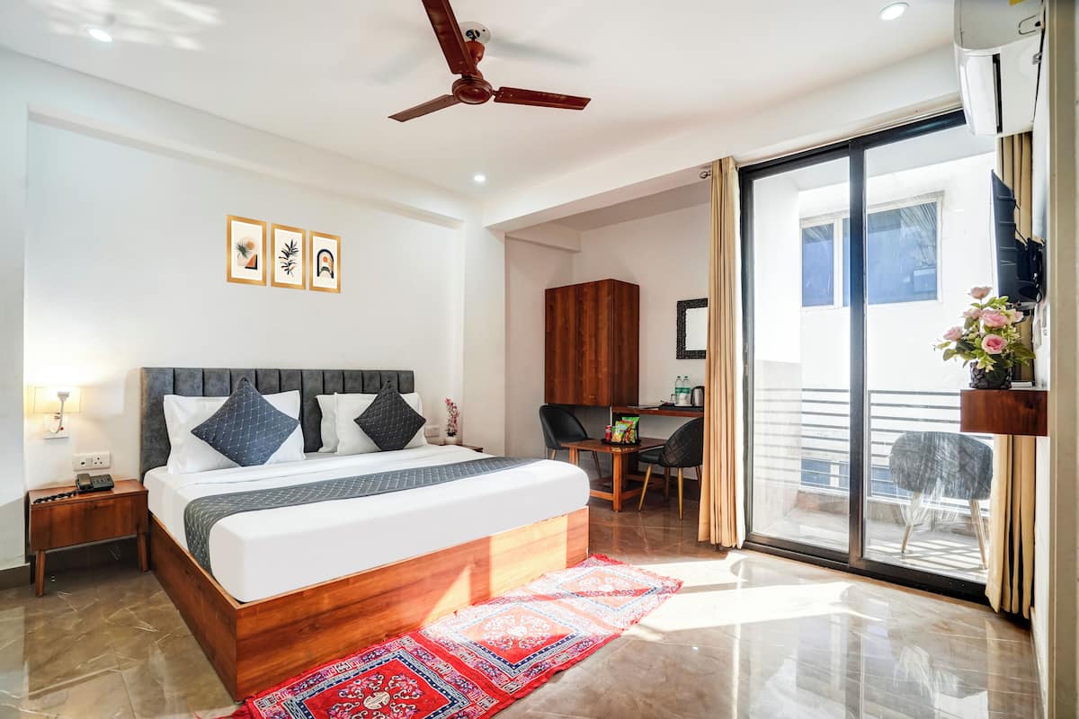 A modern hotel room with a large bed, a desk, and a balcony with a view.