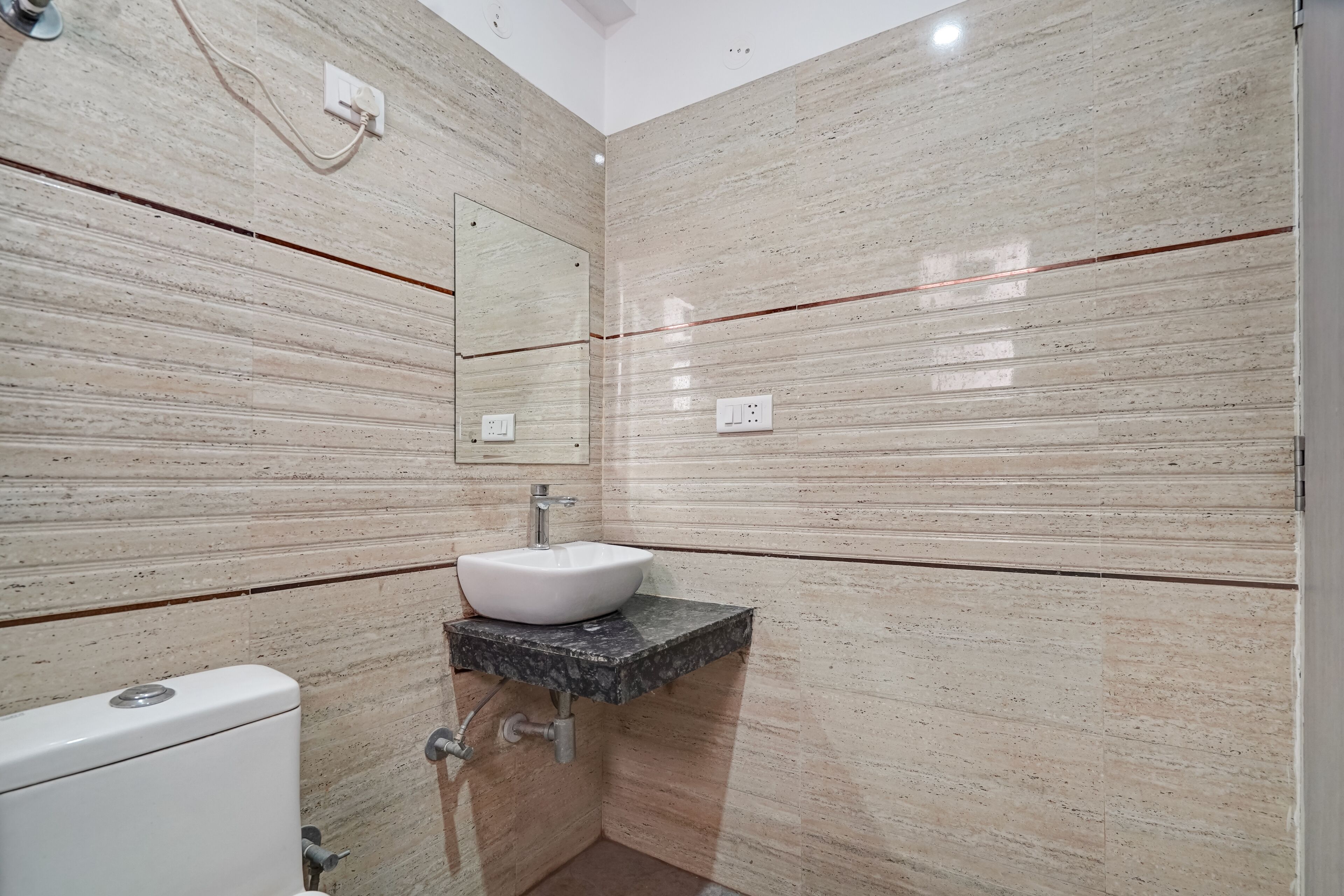 A bathroom with a marble wall, a white sink, and a toilet.