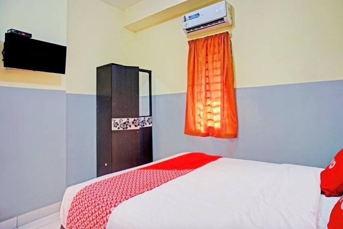 Ein Hotelzimmer mit Bett, Klimaanlage, Kleiderschrank und an der Wand montiertem Fernseher.